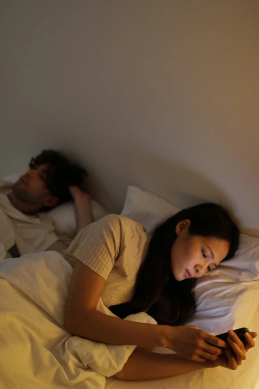 young adult couple using cell phone in bed