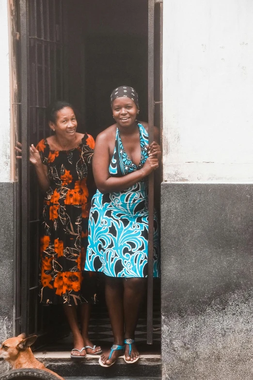 two women standing in doorway with a dog looking on