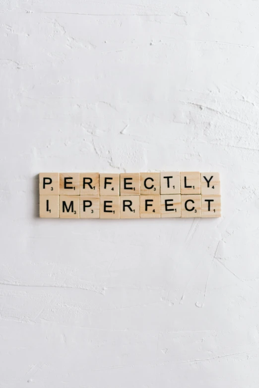 a wooden scrabble with words spelling perfectly imperfecter, on a white wall