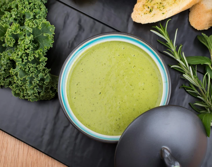 a bowl of green liquid surrounded by fresh vegetables