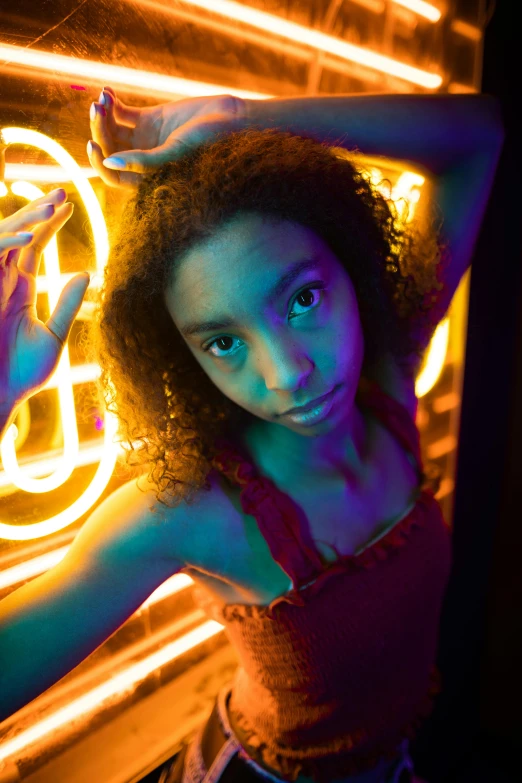 a woman with curly hair and blue eyes poses in front of neon colored wall