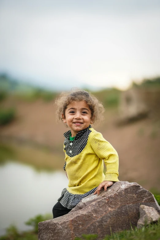 a little girl sitting on top of a rock near water
