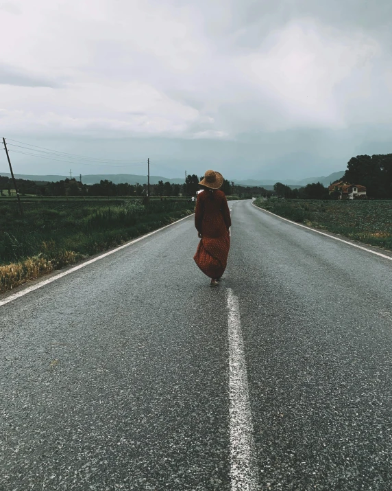 a woman walks down an empty road near mountains