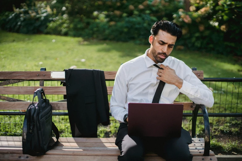 man using computer on wooden bench in park