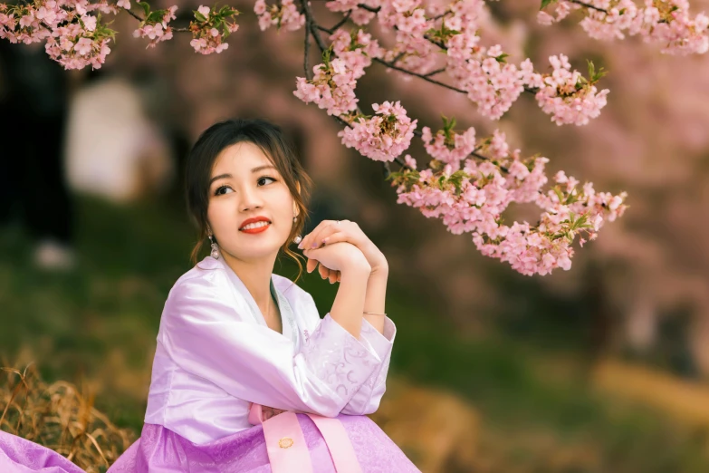 a asian woman posing in a pink dress by blossom tree