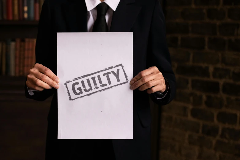 a person in a suit holds a piece of paper that says guilt