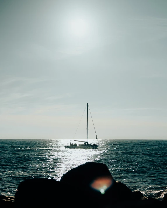 a sailboat is on the ocean in front of a rocky shoreline