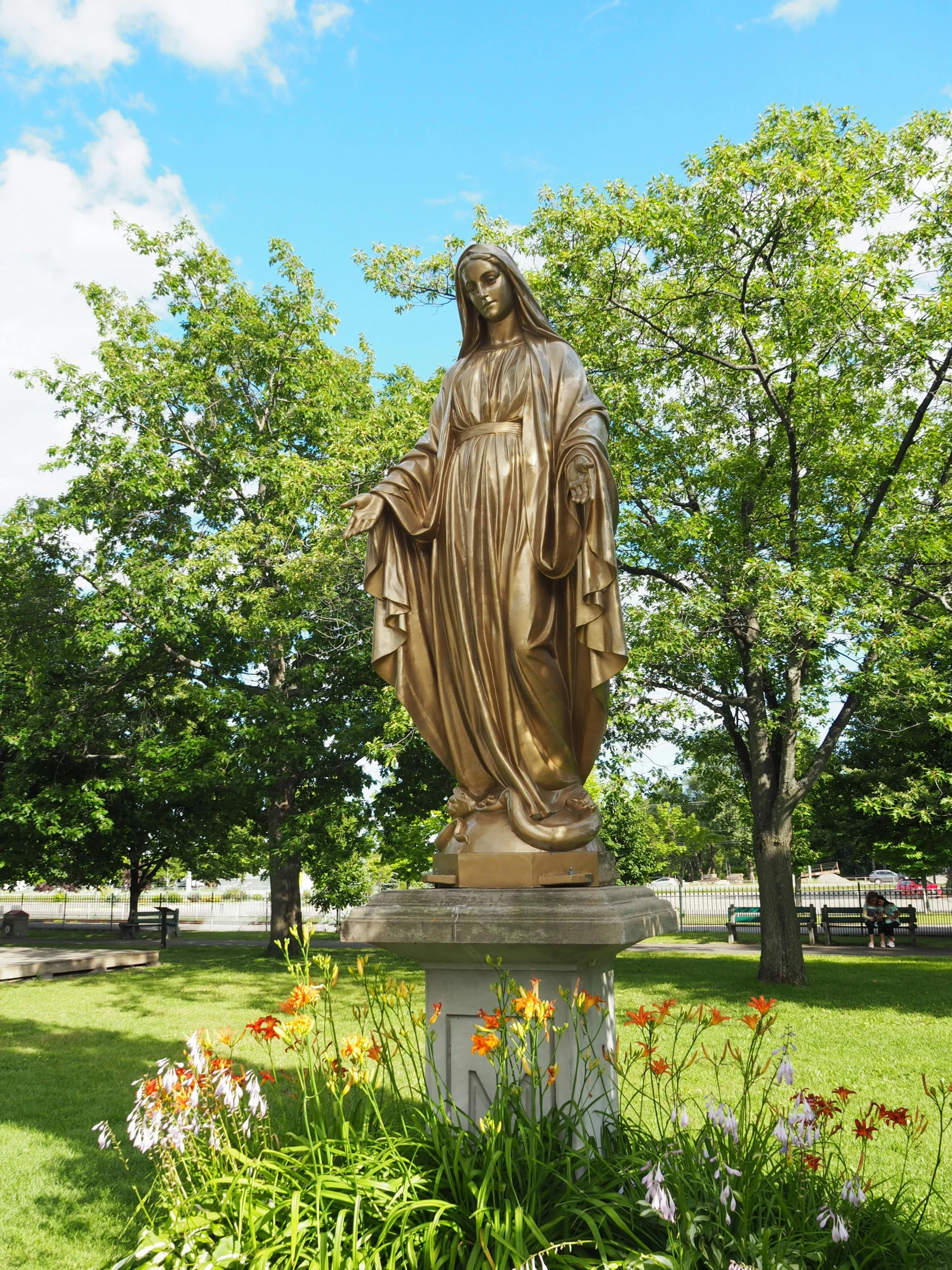 a statue of mary is in a grassy area next to a park