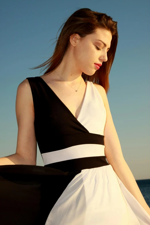 a woman with red hair wearing a black and white dress standing near the ocean