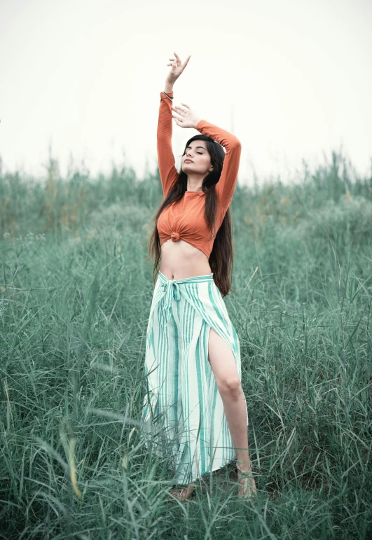 a woman poses for the camera with her arms raised up in a field