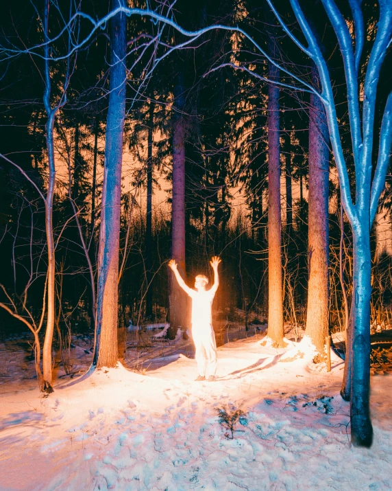 the person is standing in a snowy forest and reaching up