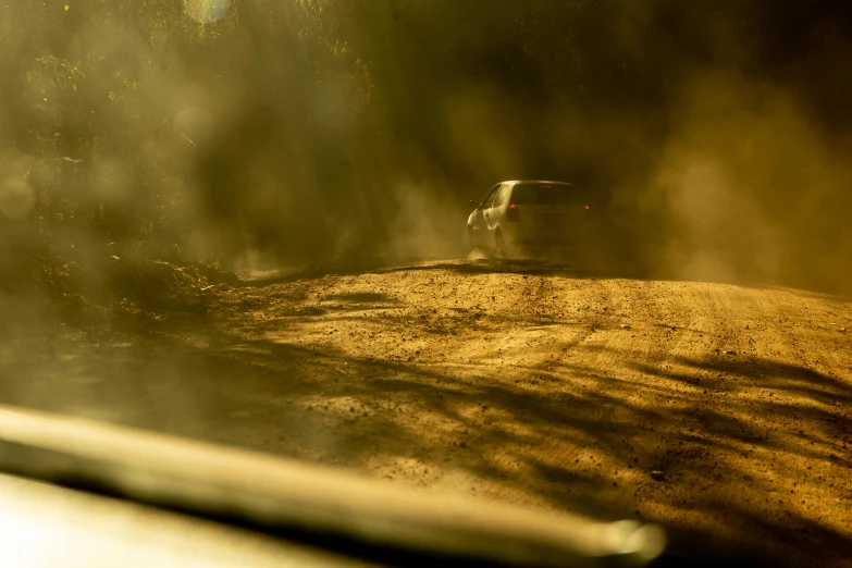 a red car is driving through the dusty road