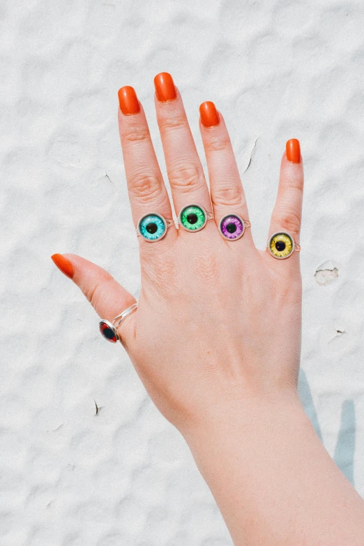 a person's hand with three rings and a multi - colored eye