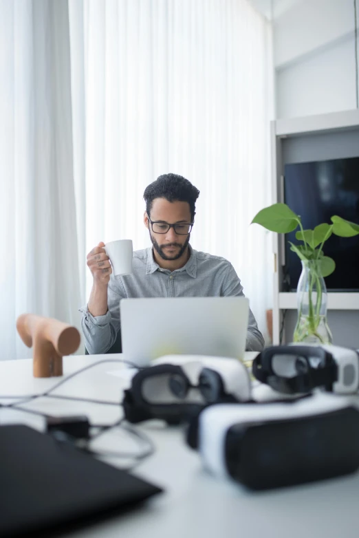 a man holding up a cup in front of his laptop