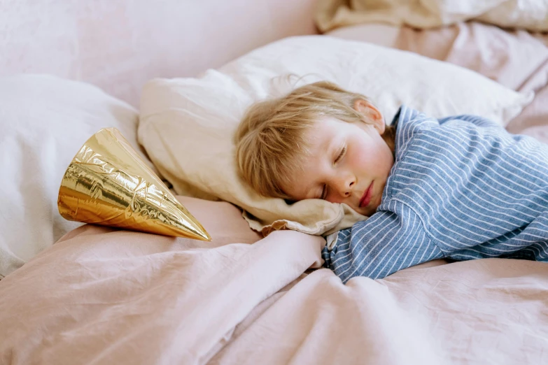 a young child sleeping on a bed with a golden cone in hand