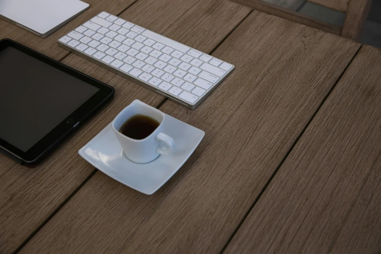 a tablet, keyboard, mouse and coffee sit on a table