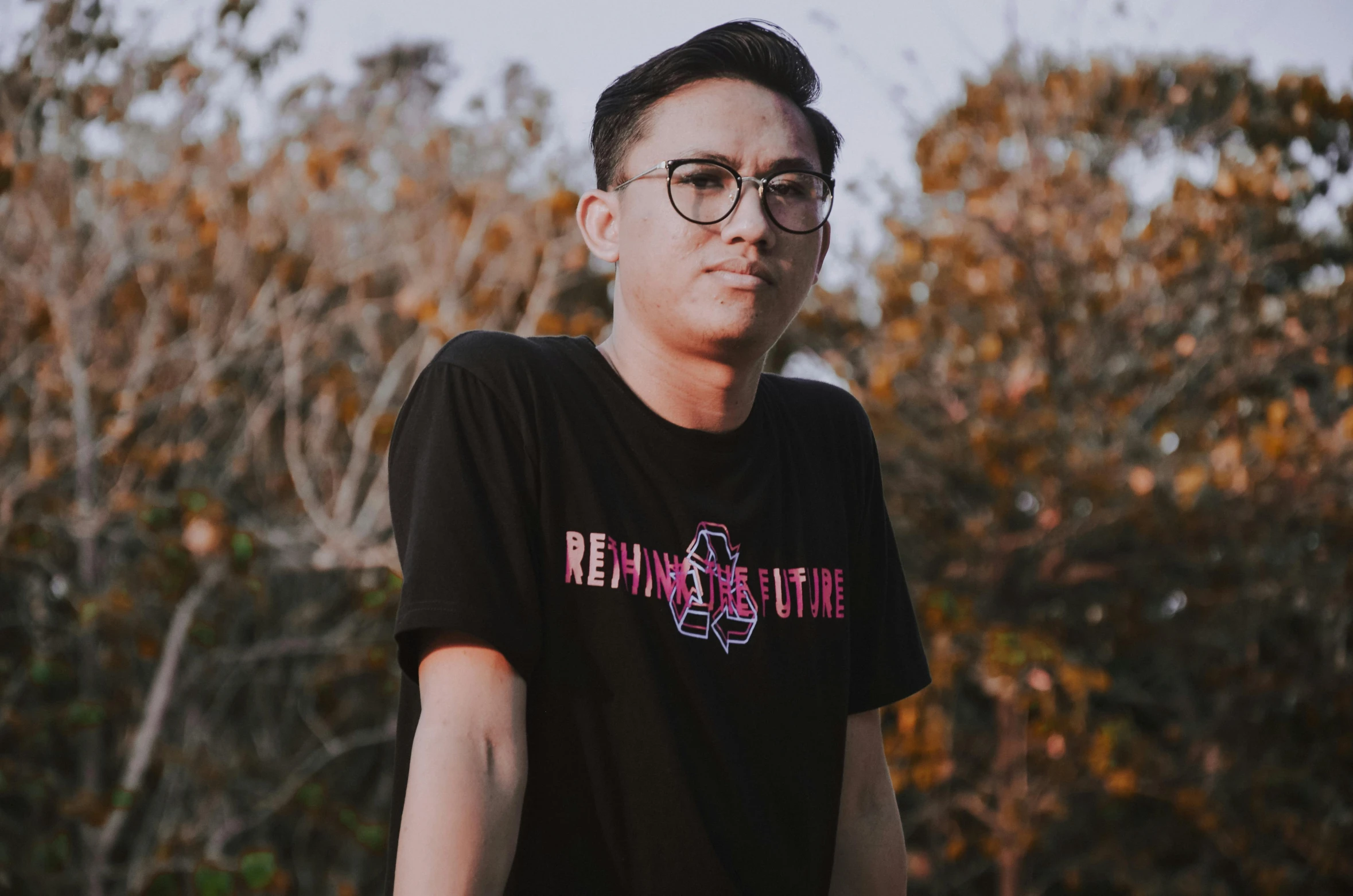 a man wearing glasses standing next to trees