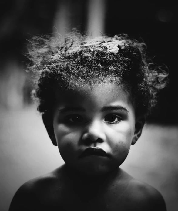 a child with curly hair standing and looking straight at the camera