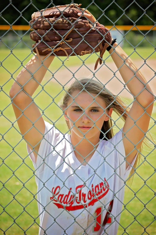 a  holding up her baseball mitt on a fence