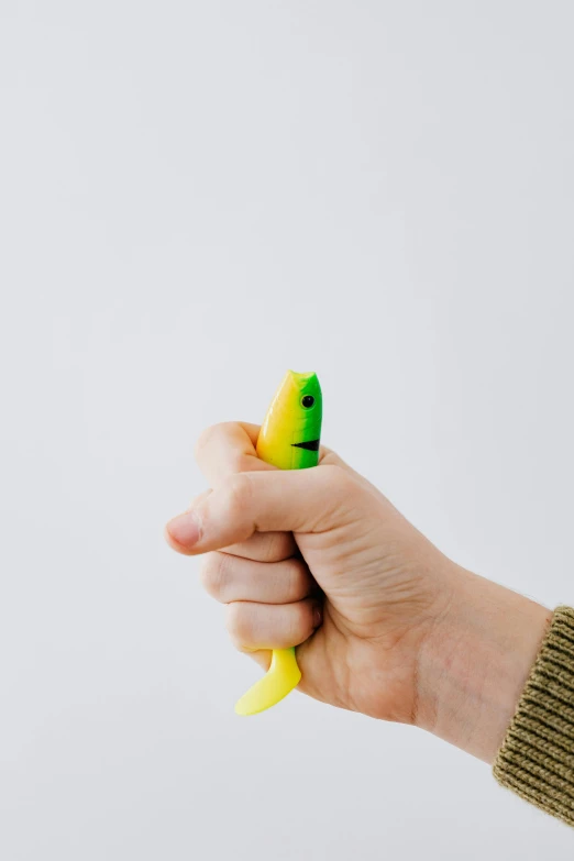 a hand holding a tiny yellow object with a face on it