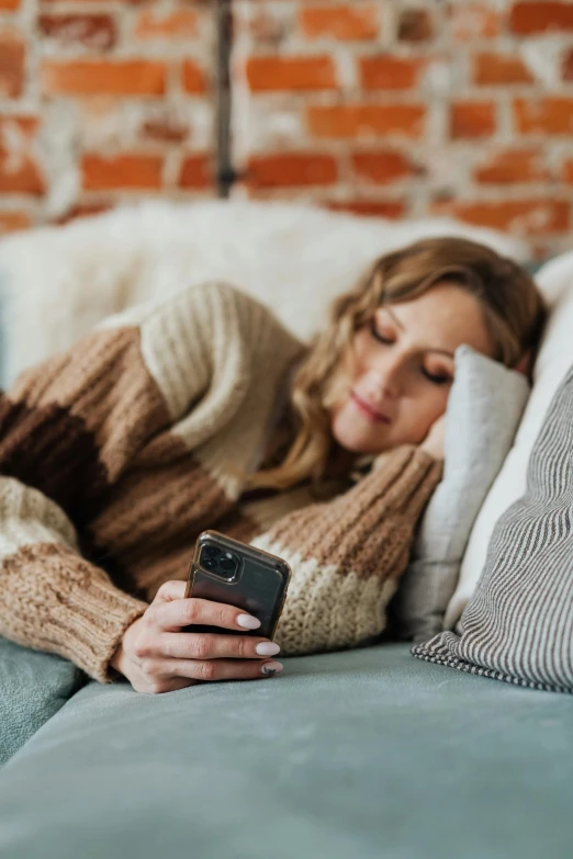 a woman lying down on a couch texting on her phone