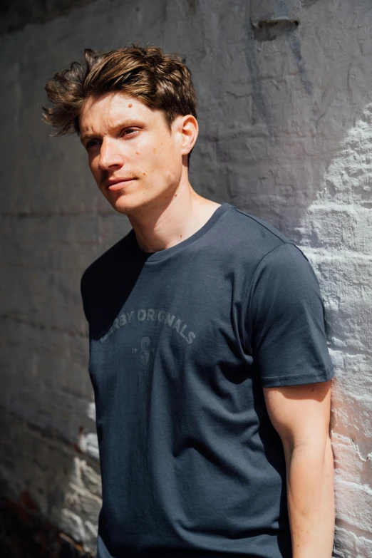 a man is posing against a brick wall