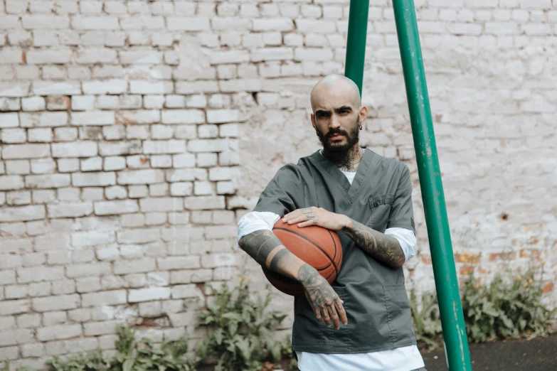 man with bald head holding basketball in front of brick wall