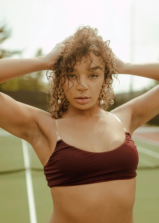 a woman wearing a maroon bikini top with her hands on her hair