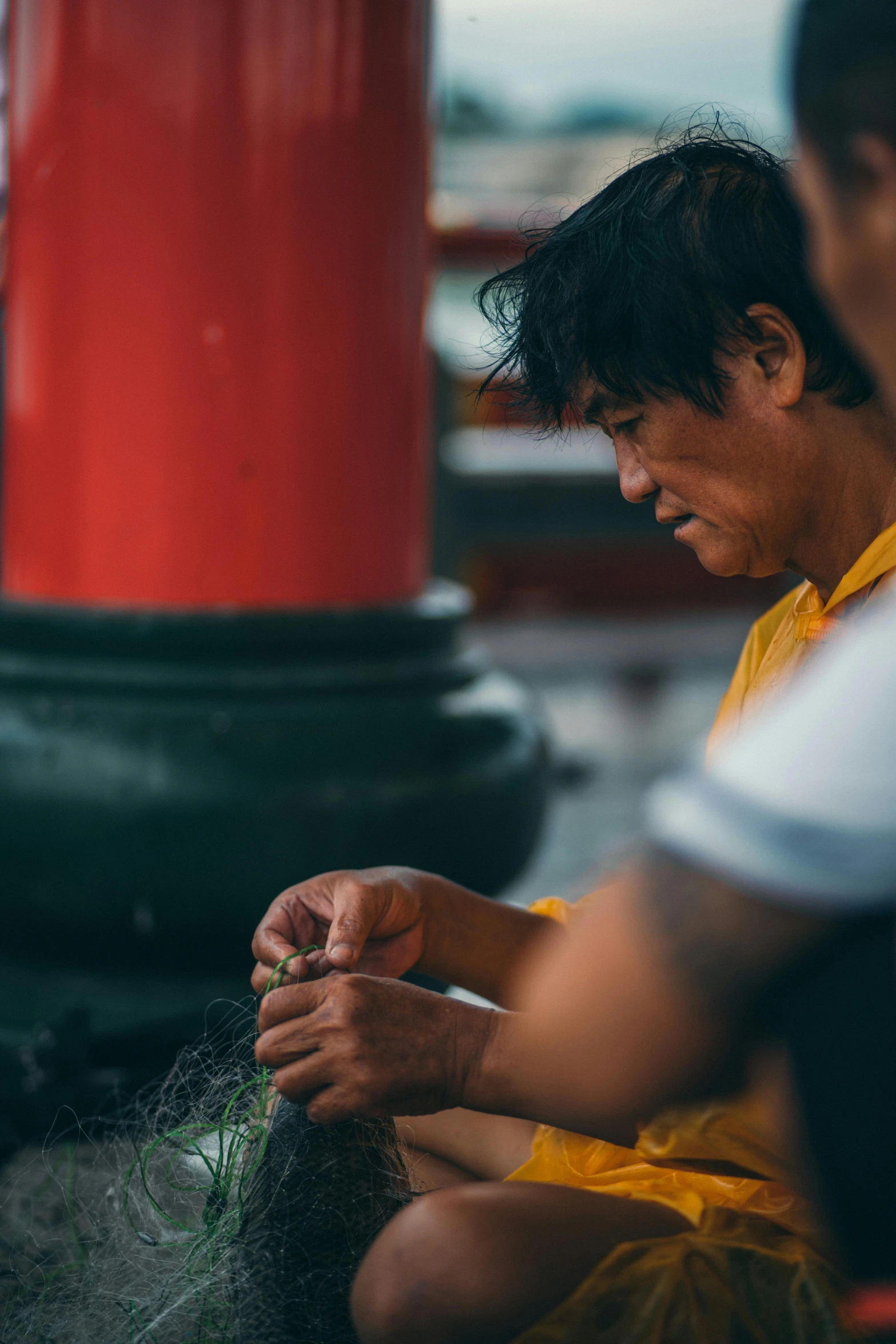 a man sitting down while knitting at an outdoor stand