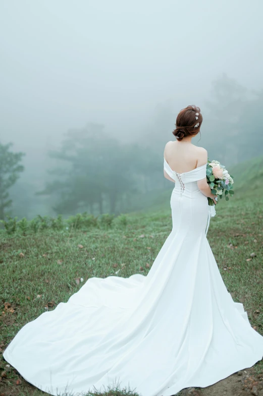 a woman is standing in a field with her back to the camera and wearing a wedding gown