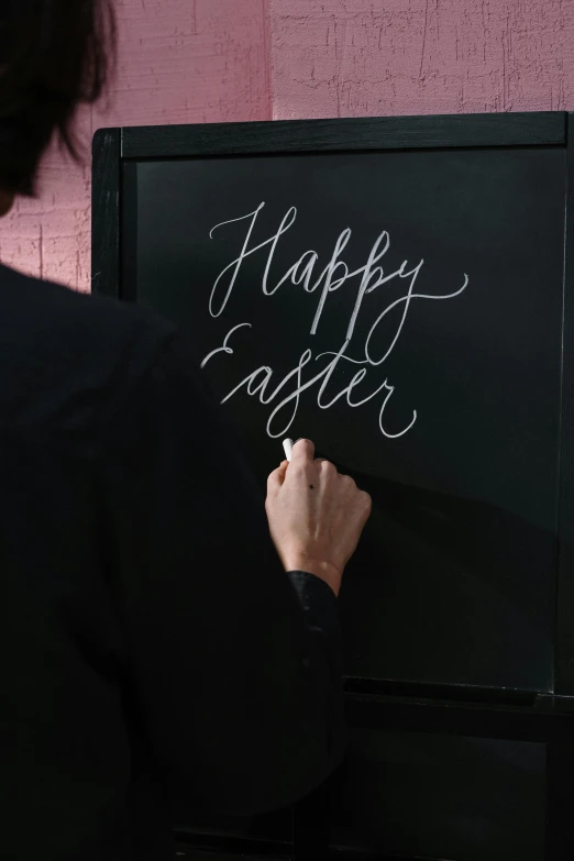 a person writing happy easter on a blackboard