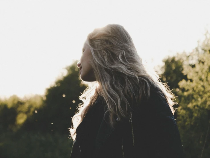 a woman standing in front of trees with long hair