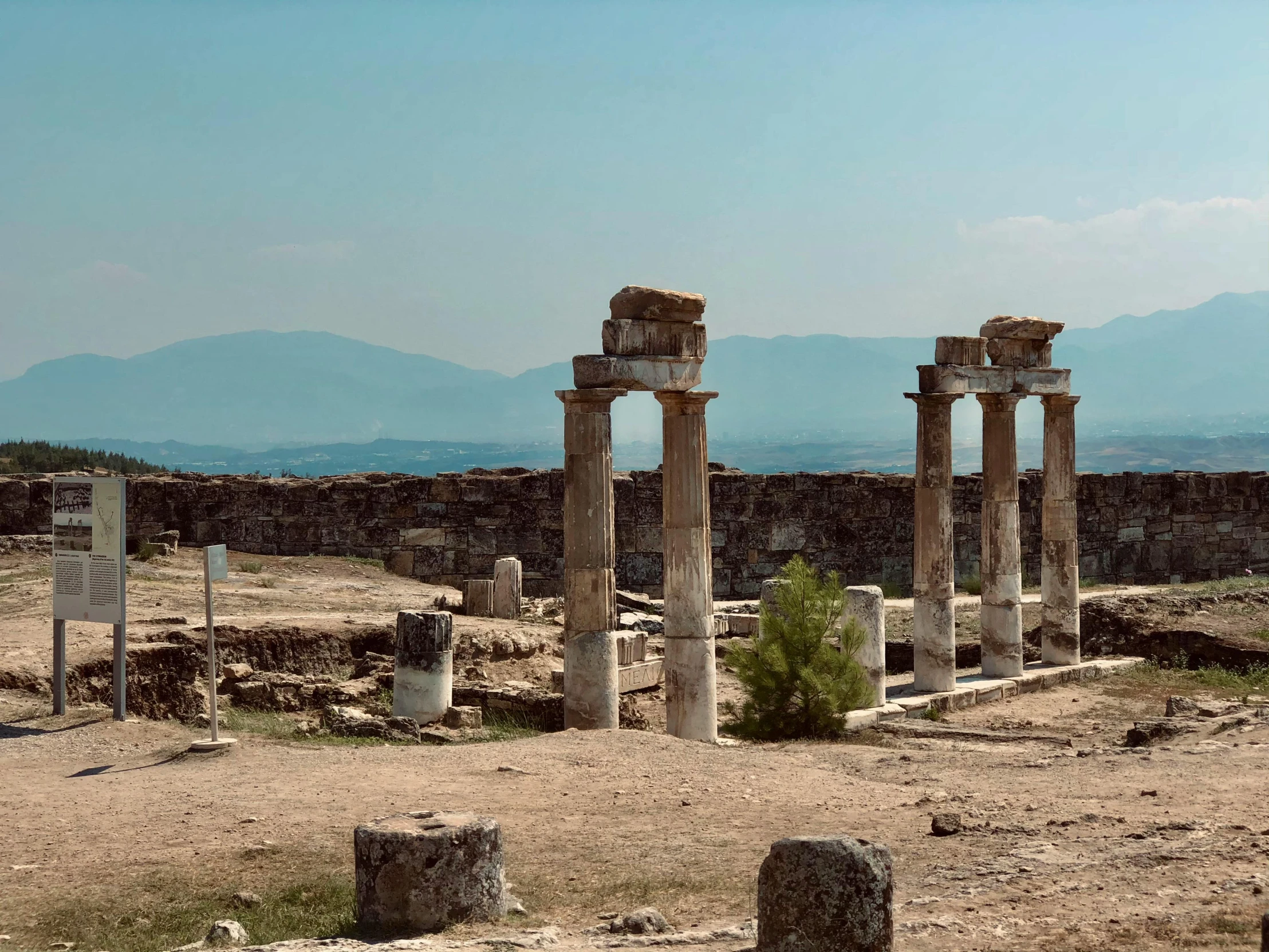 two stone pillars are near a wall with mountains in the background