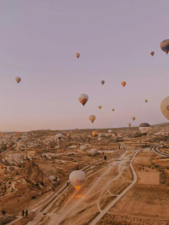 many balloons flying above some desert at sunset