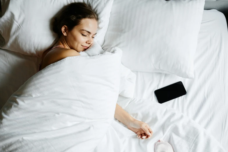 a young woman sleeps in bed with her smartphone resting on her arm