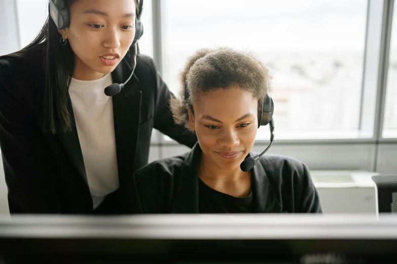 a women wearing a headset looks at a computer screen as another woman speaks on her phone