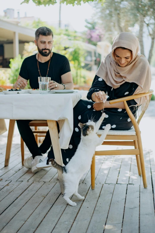 a man and woman at an outdoor restaurant with a cat