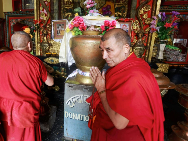 a group of monks stand by a pot with flowers in it