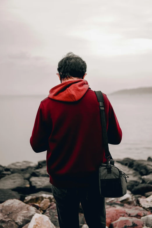 the person with a red coat and a black bag is looking over rocks