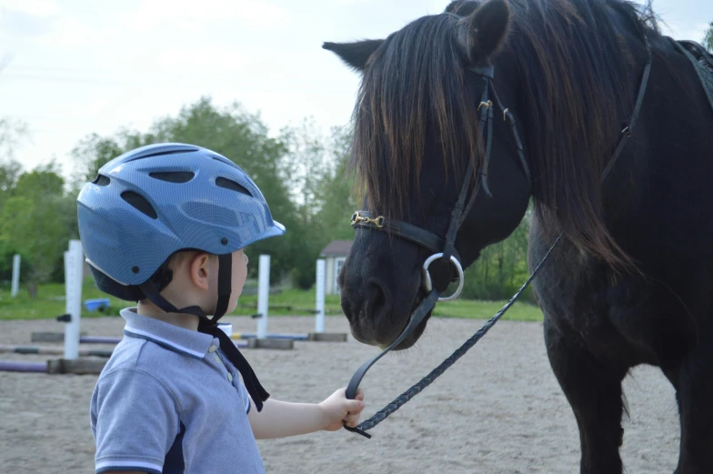 a boy in helmet standing near horse on track