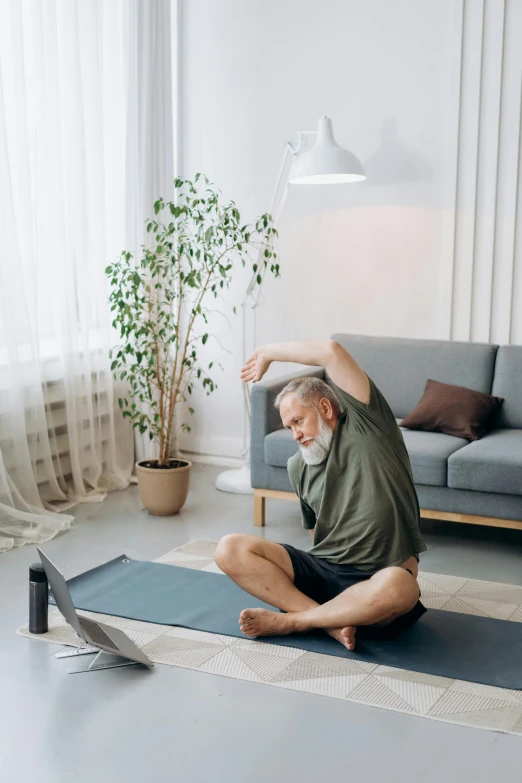 a man sitting on a mat with his legs stretched up and looking at the floor