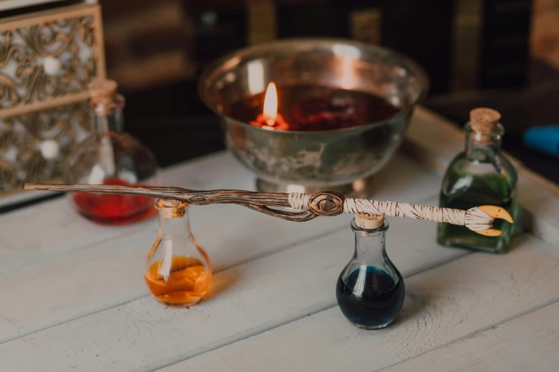 two glass bottles filled with liquid, a silver bowl with a candle and a wooden handle