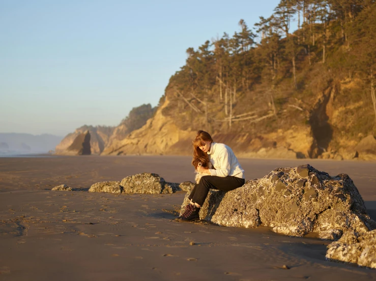 a woman sits on a rock on the beach