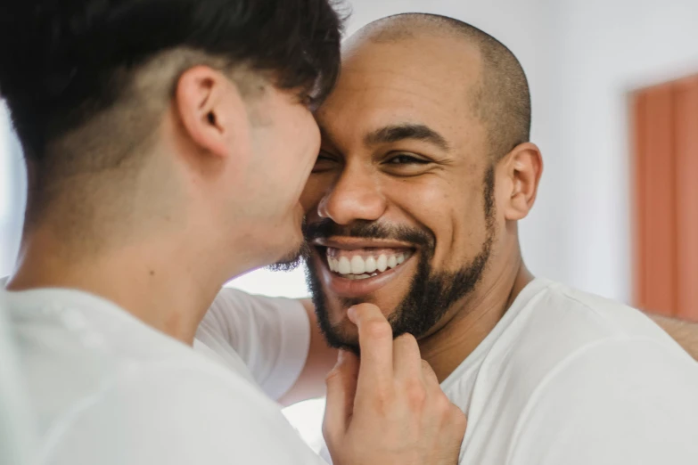 a smiling man with his finger on the cheek of a bearded man