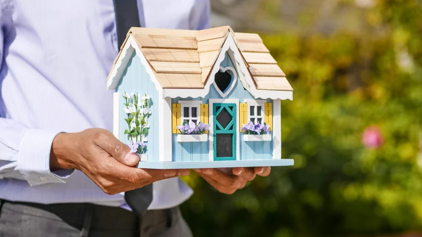 a man holding a small doll house shaped like a little cottage