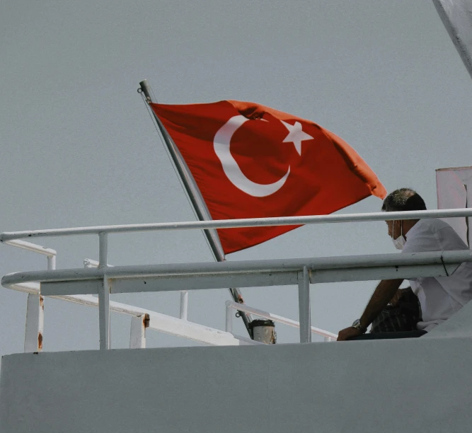 a man is sitting on the edge of the boat next to a flag