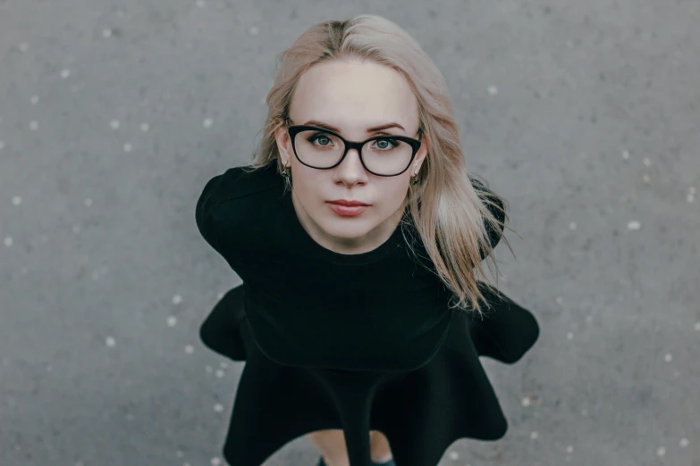 a blonde woman wearing glasses in front of a cement surface