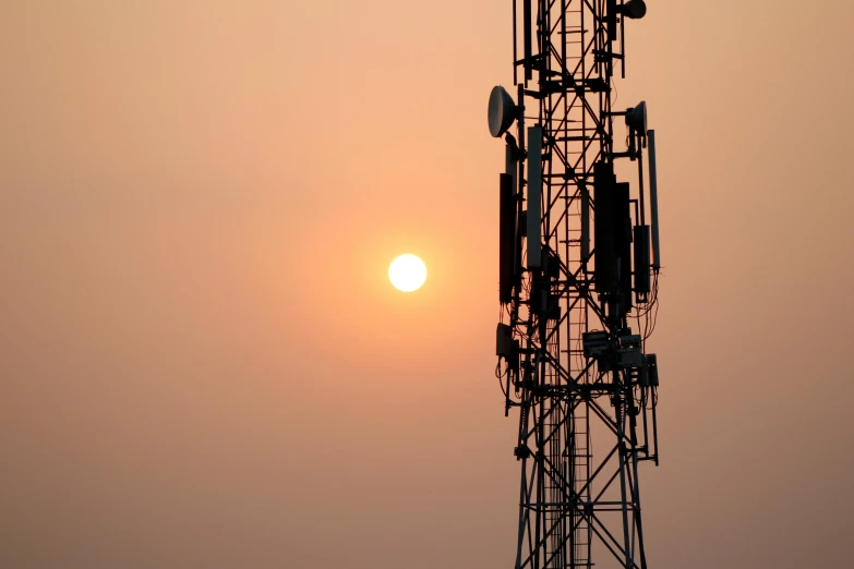 the sun peeking out through a cell tower at sunset