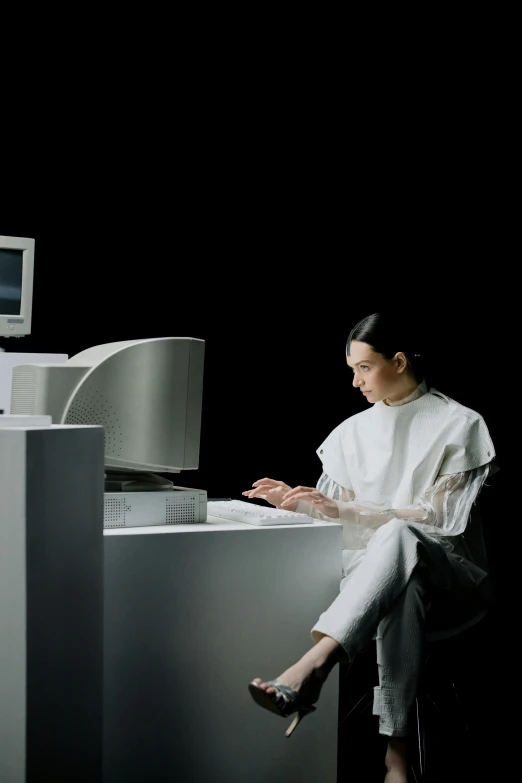 a woman in white top and pants sitting at desk