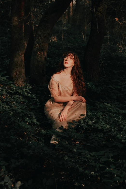 a woman sitting in the forest alone wearing a dress